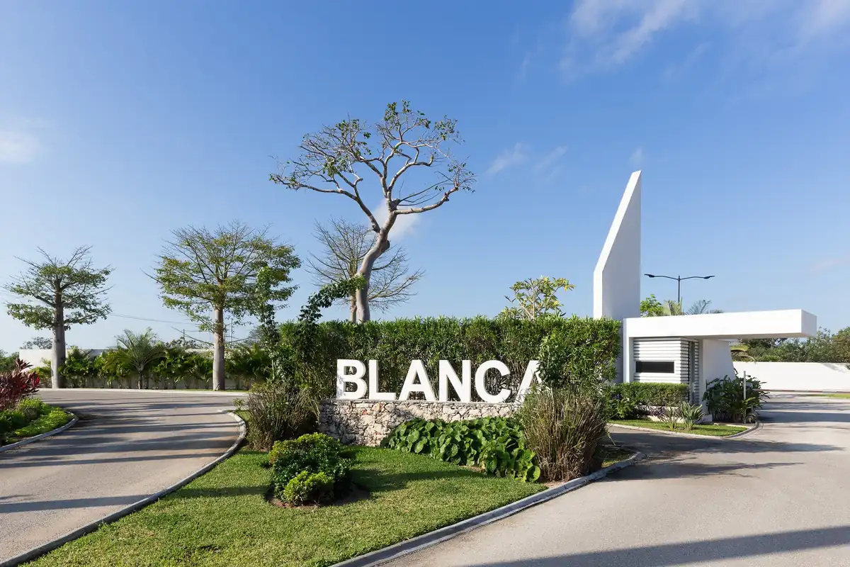 Acceso principal de Blanca Residencial con letrero, caseta y jardinería.